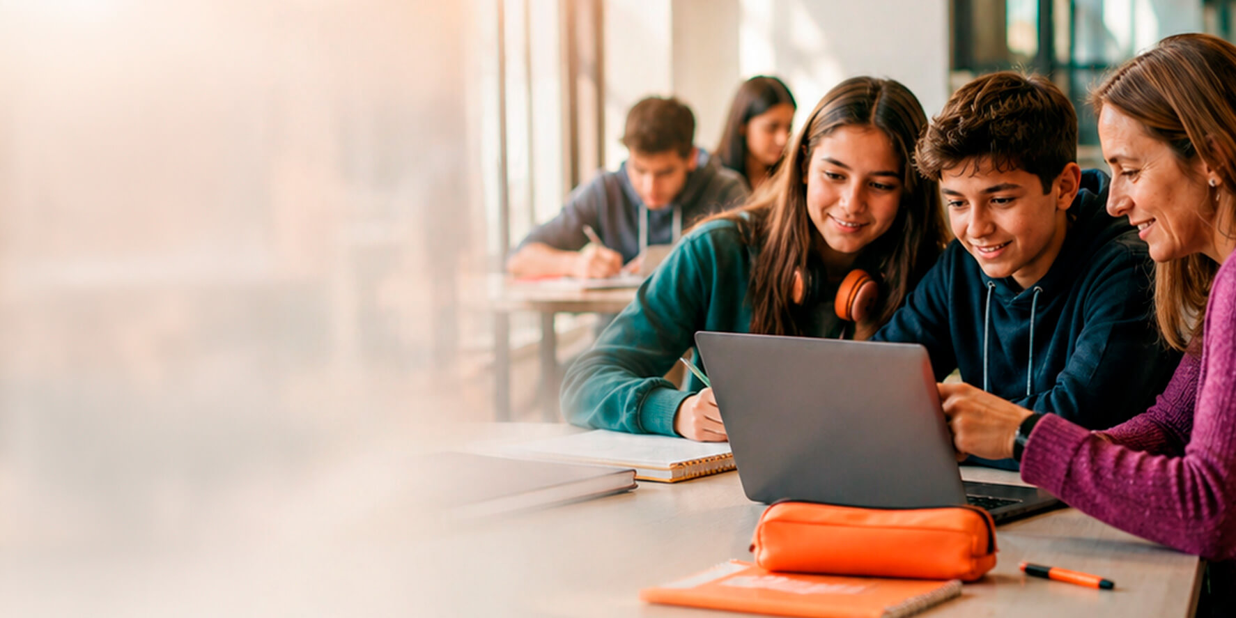 Docente acompañando a dos estudiantes que trabajan juntos en una notebook durante la clase